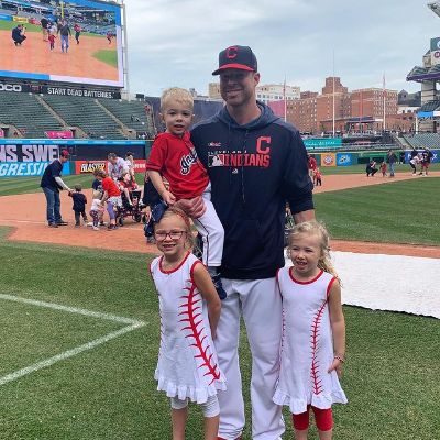 Corey Kluber is carrying Kennedy Kluber whereas Kendall and Camden Kluber are standing in front of her for the picture.